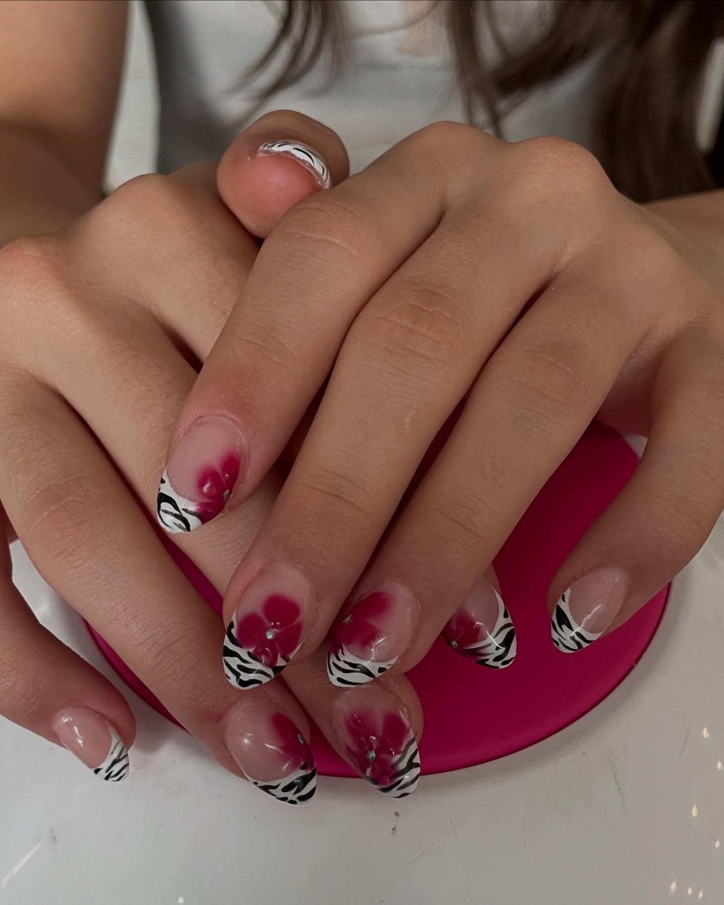 Short rounded nails with zebra-print French tips and airbrushed magenta blossoms dotted with tiny silver gems on a sheer base