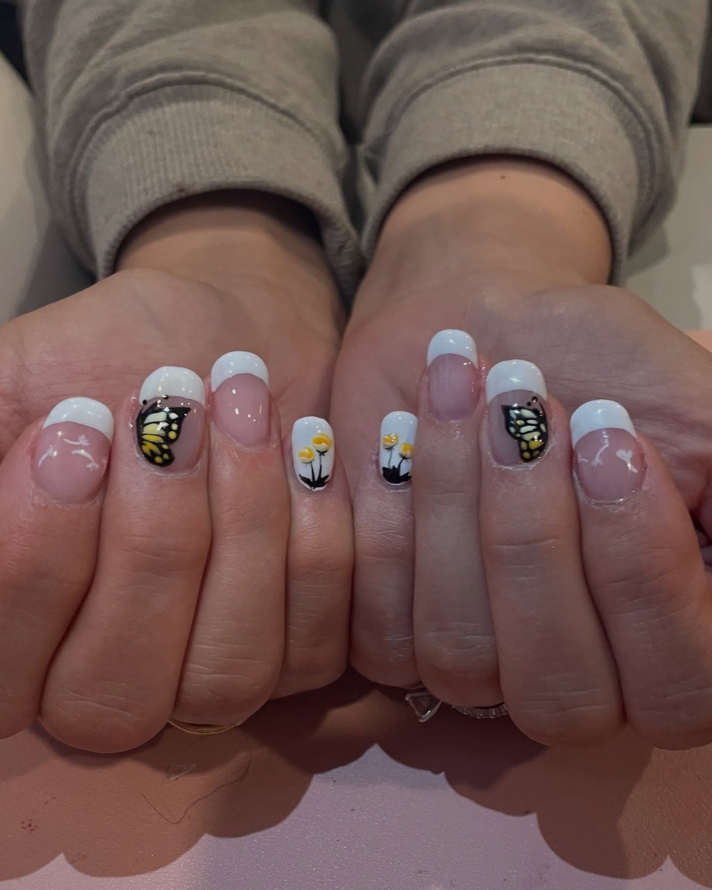 Short squoval nails with clean white French tips, accented by monarch butterfly wings and hand-painted yellow buttercups