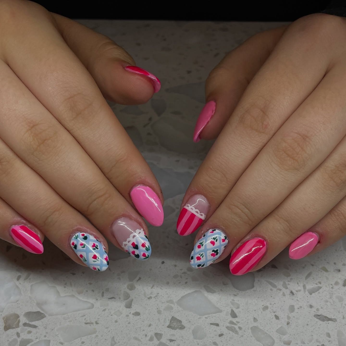 Almond nails mixing candy-pink stripes, solid pink and a pale blue lattice pattern dotted with tiny rosebuds and lace trim