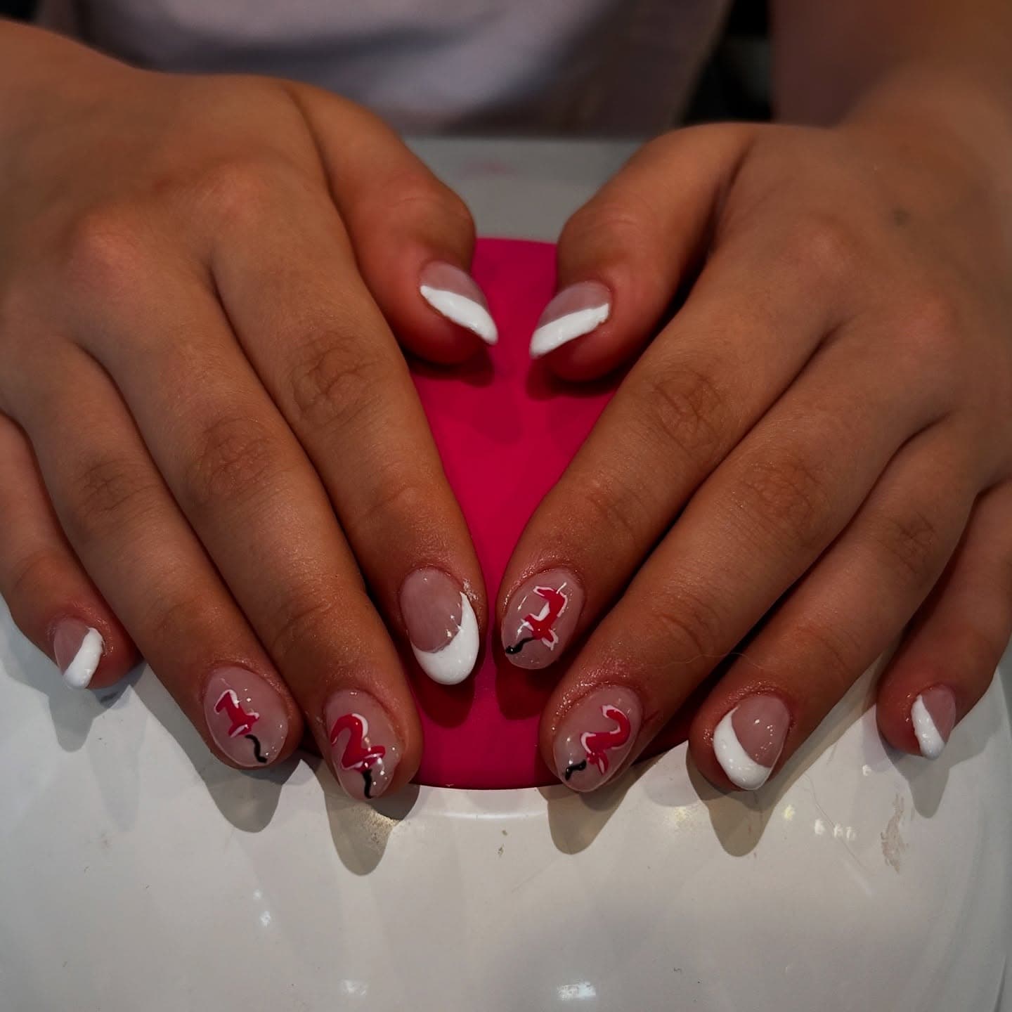 Short almond nails in sheer pink with sweeping white French tips and a hand-painted red number twelve on the accent nails
