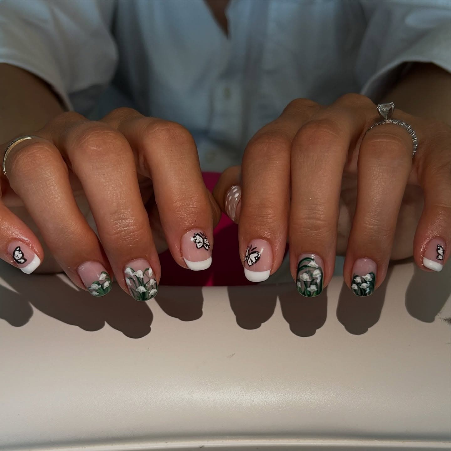 Short square nails with white French tips, hand-painted lily of the valley sprigs and delicate black-and-white butterflies
