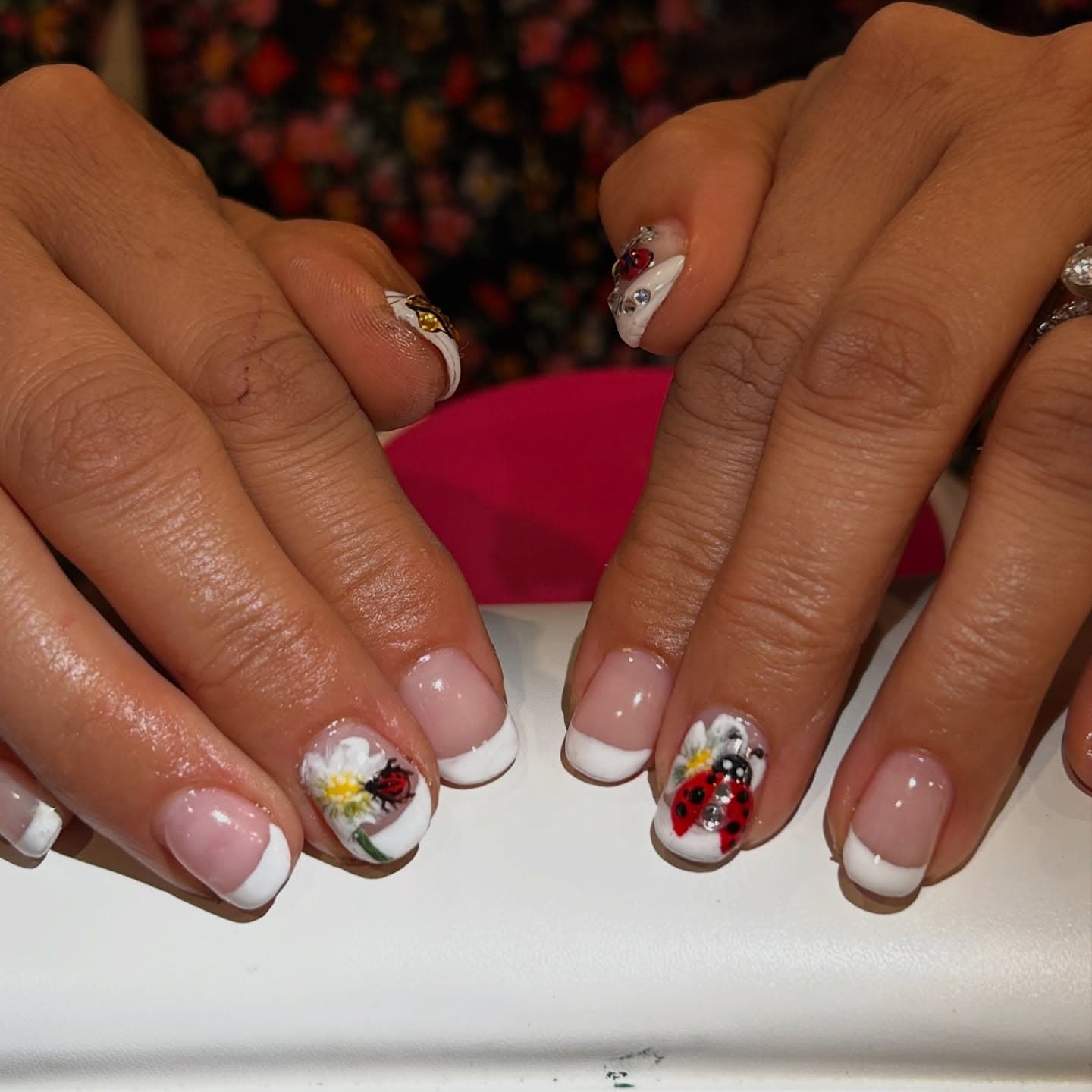 Short natural nails with white French tips and a hand-painted daisy accent topped by a 3D ladybug and tiny crystals