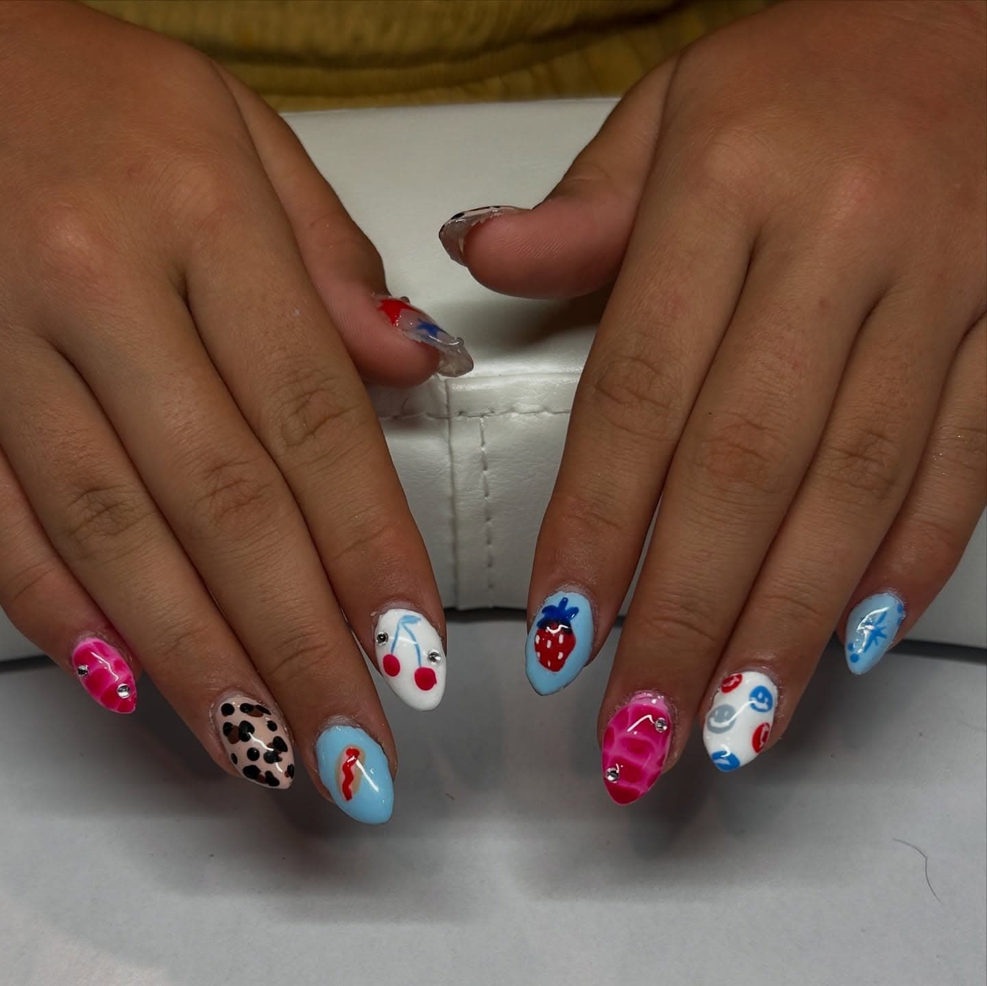 Almond nails in a playful Y2K mix of pink crocodile texture with gems, leopard print, cherries, a strawberry and tiny smiley faces