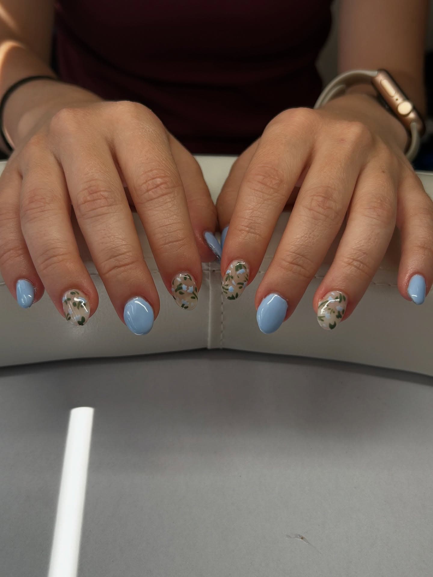 Short almond nails alternating solid baby blue with sheer accents of hand-painted blue tulip sprigs and green leaves