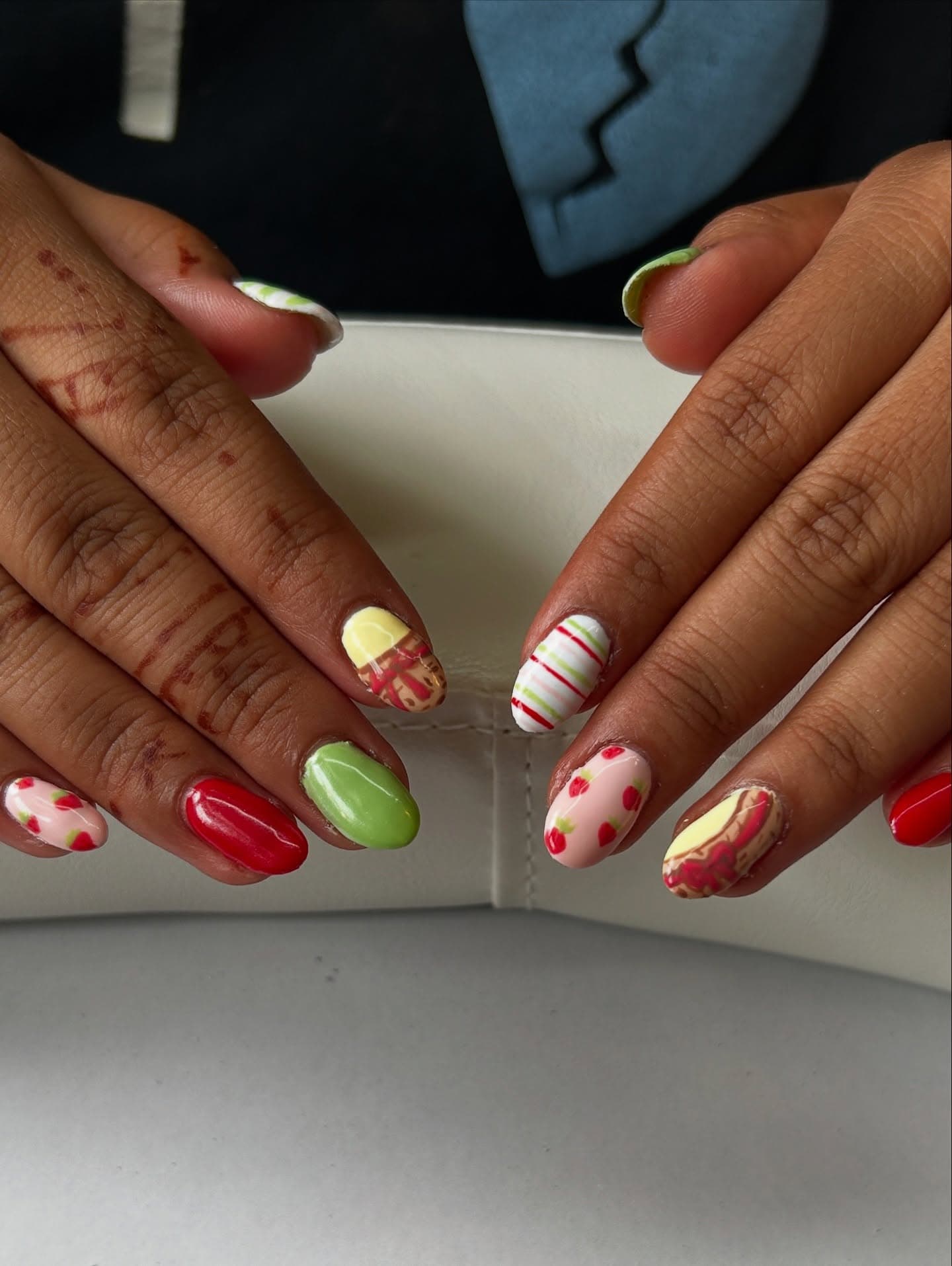 Henna-adorned hands with oval nails in a strawberry picnic set of red, pistachio green, candy stripes and bow-wrapped pastry accents