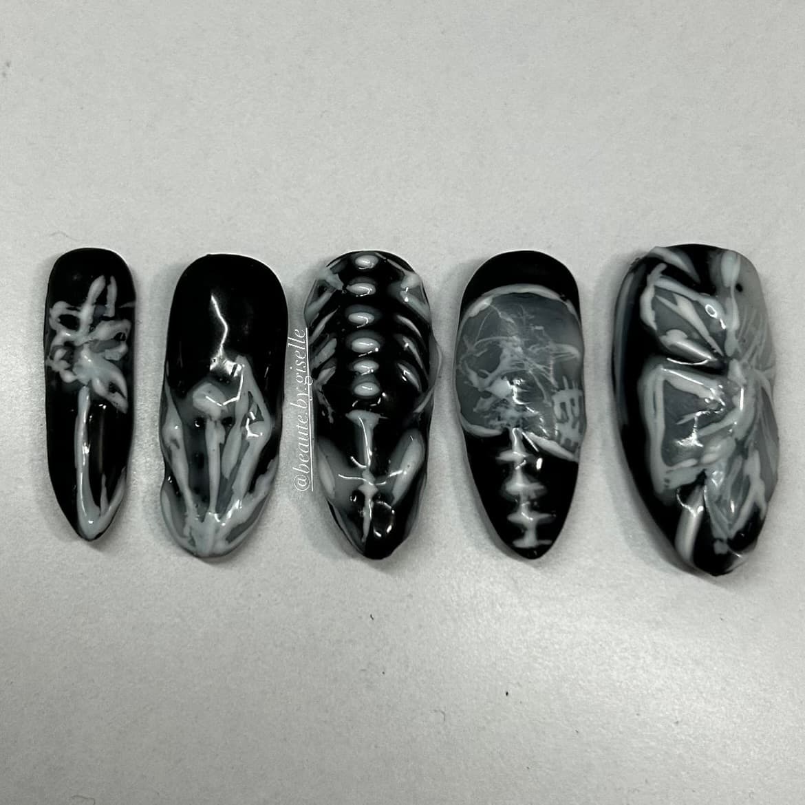 A set of black almond press-on nails hand-painted with eerie white skeleton art including a skull, ribcage and moth for Halloween