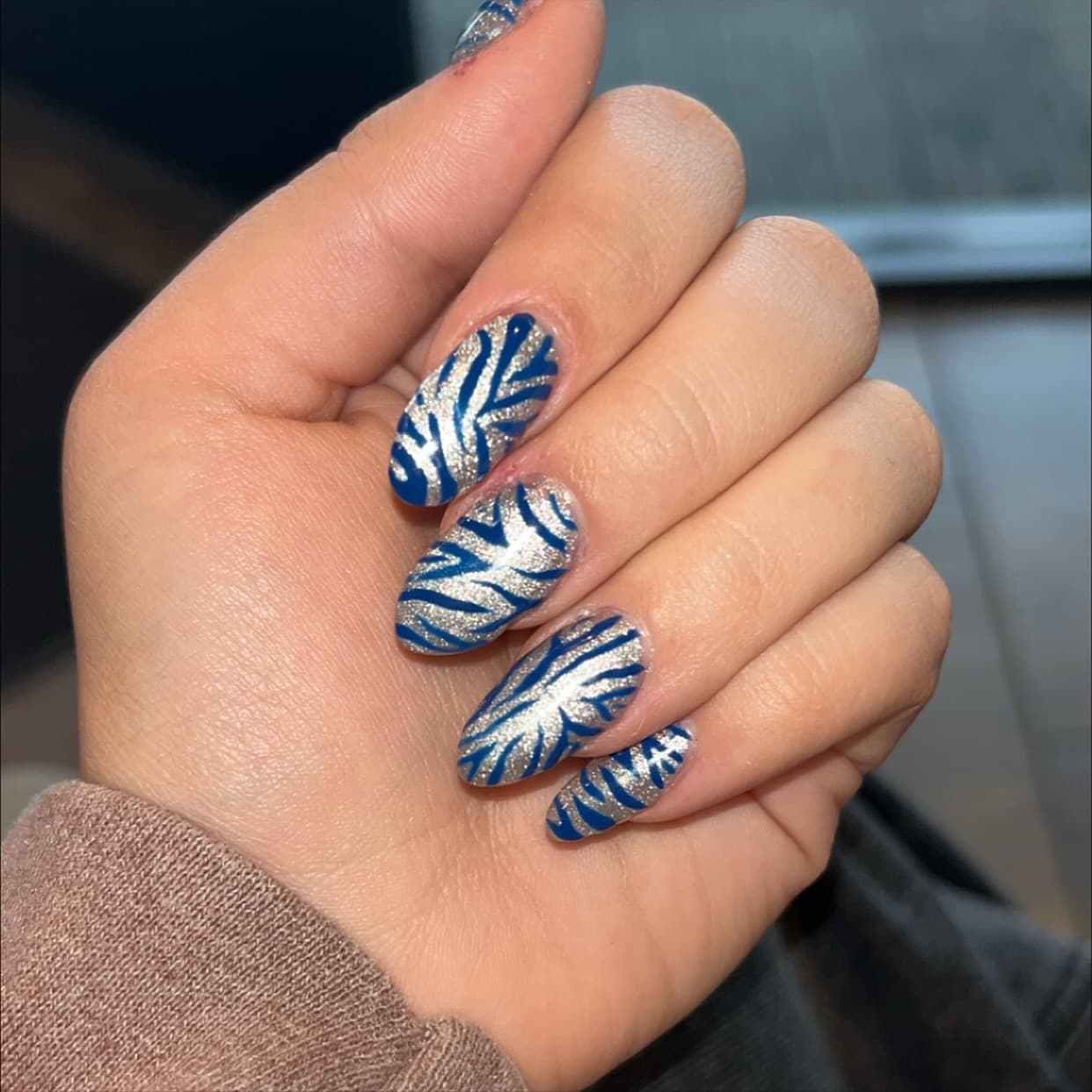 Almond nails in champagne glitter cat-eye overlaid with bold cobalt-blue zebra stripes