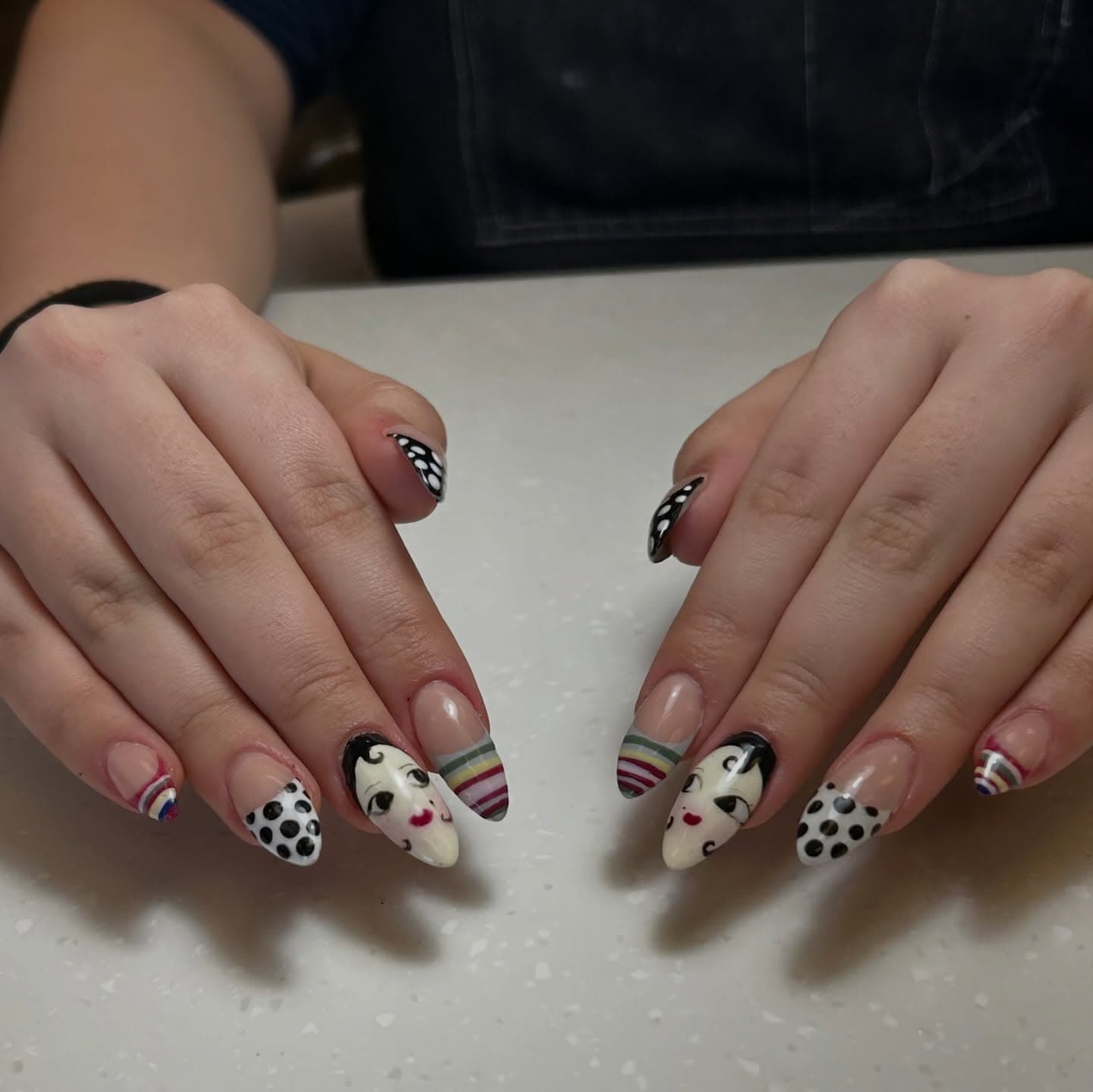 Almond nails in sheer nude with hand-painted flapper doll faces, black-and-white polka dots and striped rainbow French tips